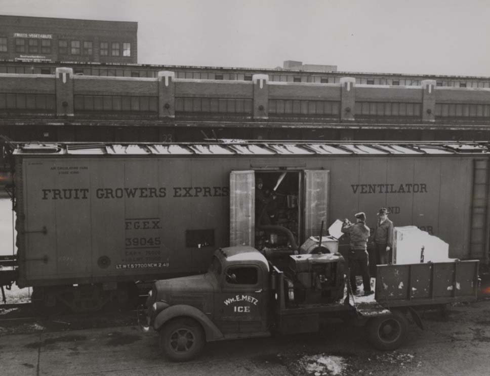 Men loading ice blocks into railcars of wholesale produce near produce terminal, c1917-c1930. 